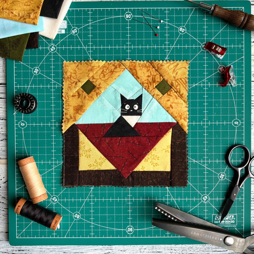 Whimsical Cat quilt block pattern displayed on a green cutting mat with sewing tools and thread