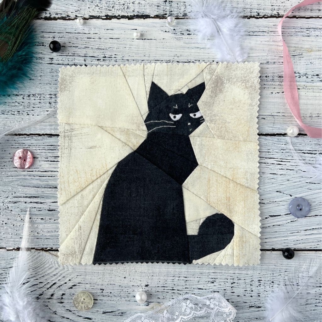 What black cat quilt block pattern featuring a sassy black cat on soft cream background styled with feathers and buttons