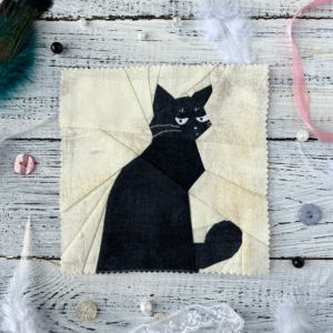 What black cat quilt block pattern featuring a sassy black cat on soft cream background styled with feathers and buttons
