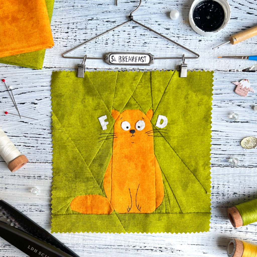 5th Breakfast ginger cat quilt block pattern on green background with sewing tools and hanger display