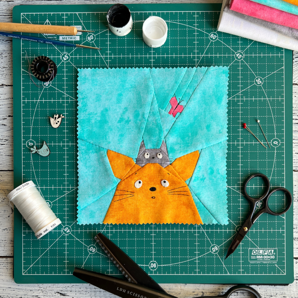 Curious Cats quilt block pattern featuring a ginger cat and gray cat looking upward on aqua background