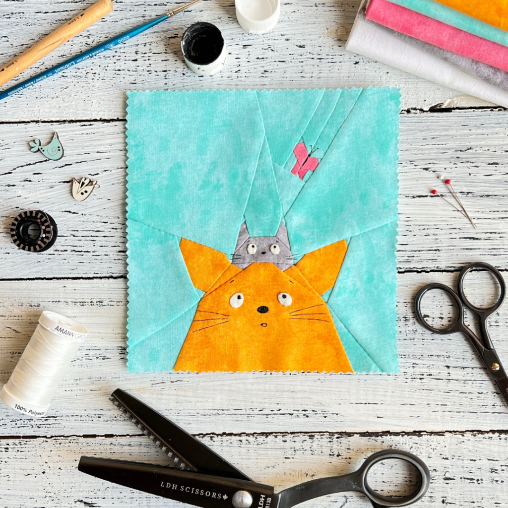 Curious Cats quilt block pattern featuring a ginger cat and a gray cat looking up at a pink butterfly on an aqua background