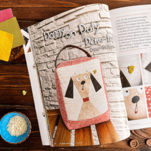 Open magazine spread featuring the Doggy on Duty dog door stopper project on a wooden table with fabric swatches and rice bowl