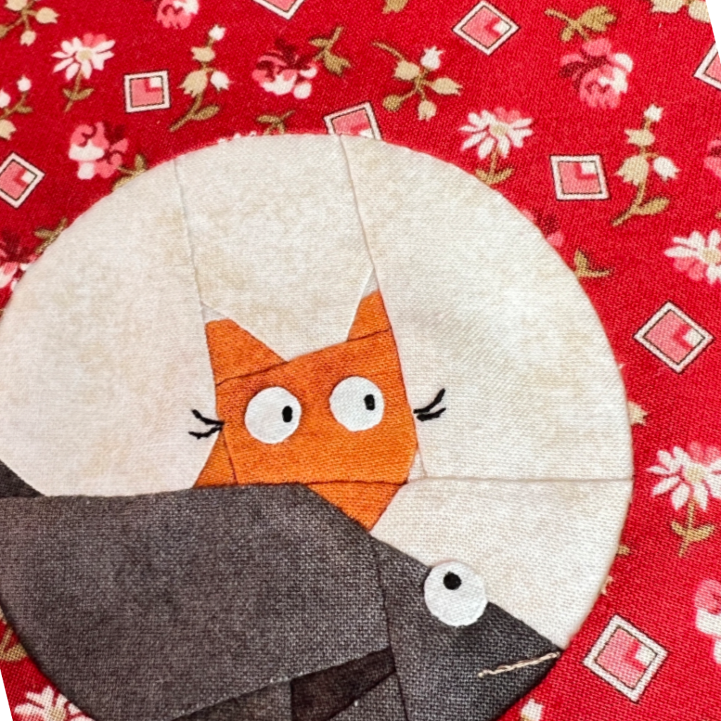 Close-up of Dream Big cat quilt block showing kitty face and large fish detail on red floral background