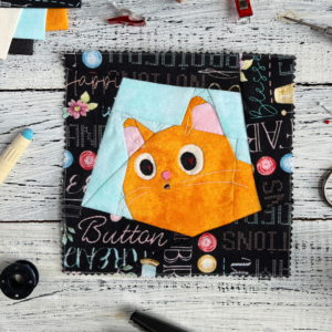 Love Is in the Eyes ginger cat quilt block pattern featuring a curious cat peeking from a box on sewing themed fabric background