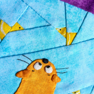 Close-up of Make a Wish cat quilt block showing ginger cat face and fish details on blue pieced fishbowl background