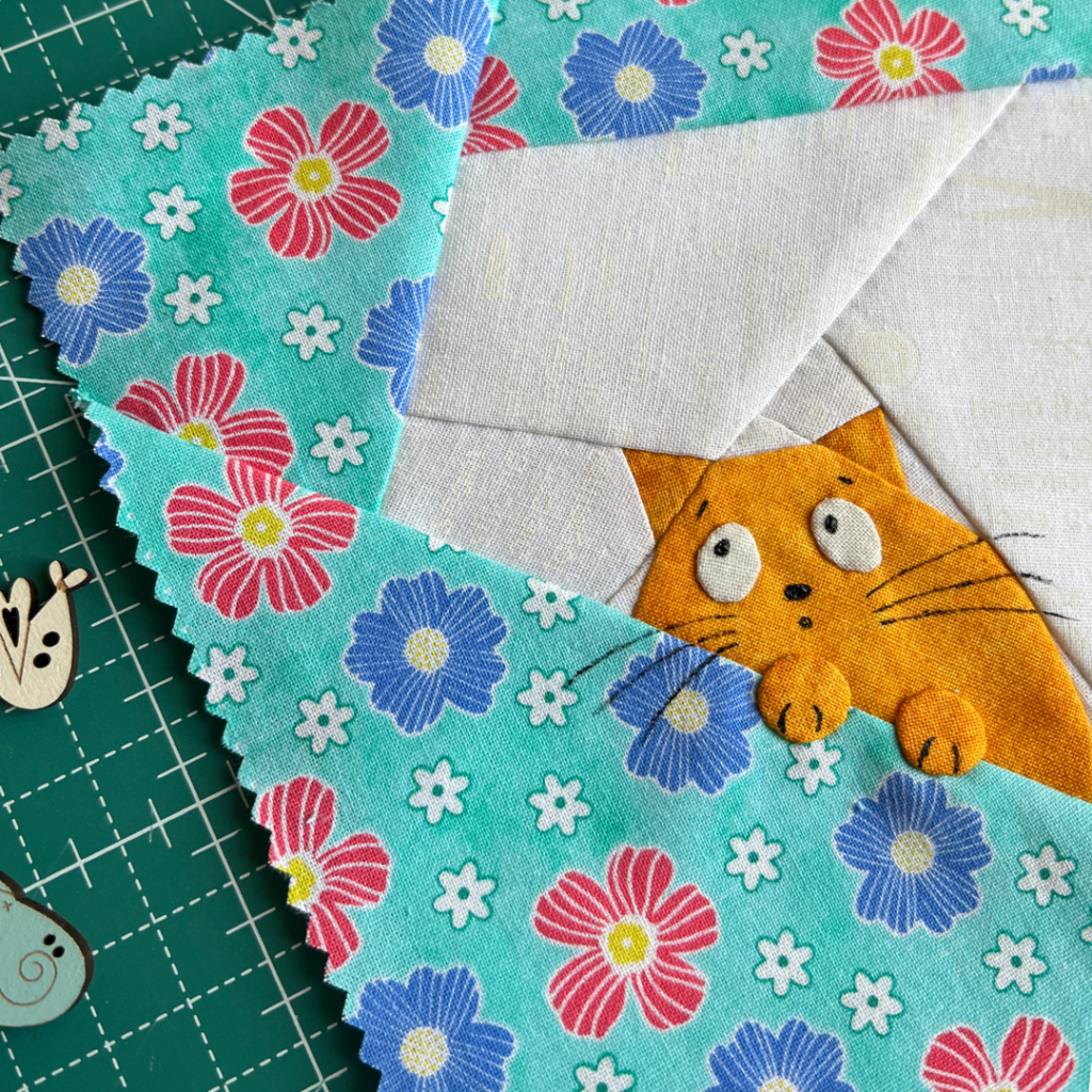 Close-up of Peek-a-boo ginger cat quilt block showing face paws and floral fabric detail