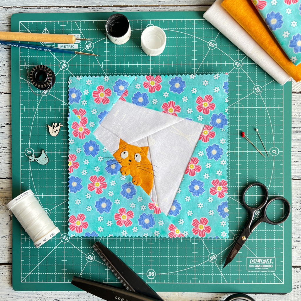 Peek-a-boo ginger cat quilt block pattern featuring a ginger cat peeking out on aqua floral background