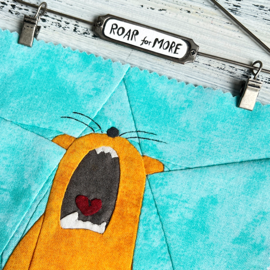 Close-up of Roar for More ginger cat quilt block showing appliqué face detail on turquoise patchwork background